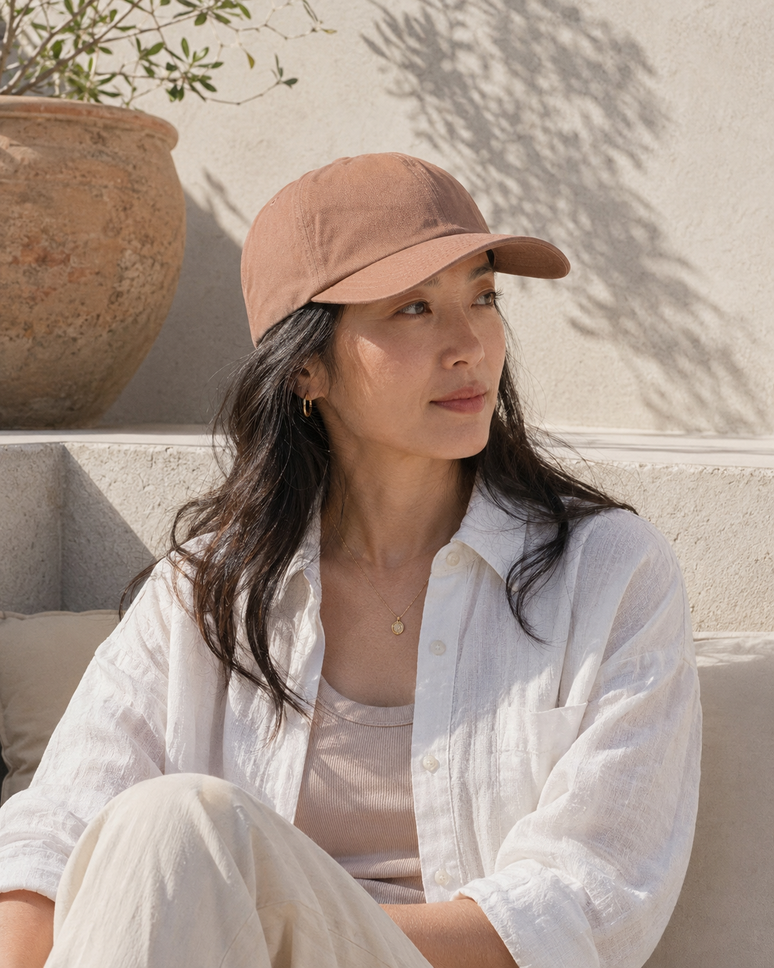 Woman wearing a brown cap sitting outdoors with a neutral background