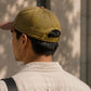 Person wearing a green cap and beige shirt against a neutral background