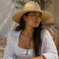 Woman wearing a straw hat and white shirt sitting outdoors.