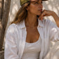 Woman wearing a white shirt and beige pants with a green cap, sitting outdoors.
