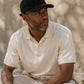 Man wearing a black cap and white shirt sitting outdoors.