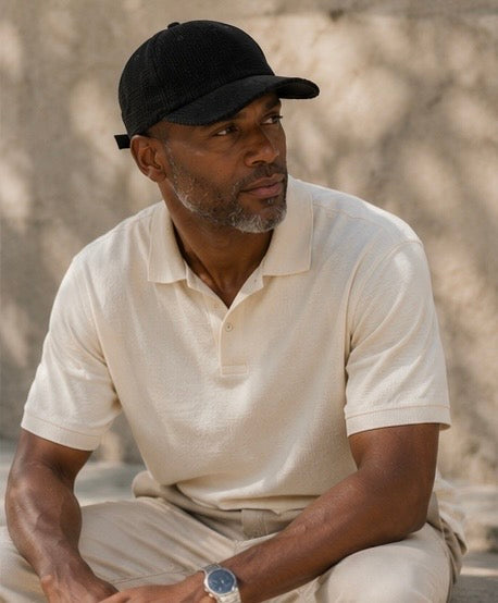 Man wearing a black cap and white shirt sitting outdoors.