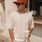 Man wearing a white t-shirt and orange cap, holding a coffee cup outdoors.