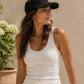 Woman wearing a black cap and white tank top against a beige wall.