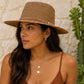 Woman wearing a brown hat and top against a stone wall with a cactus plant.