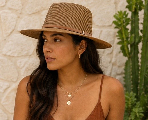 Woman wearing a brown hat and top against a stone wall with a cactus plant.