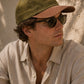 Man wearing a green cap and sunglasses against a neutral background
