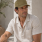 Man wearing an olive green cap and light-colored shirt sitting outdoors.