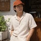 Man wearing an orange cap and beige shirt standing in a casual setting.