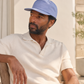 Man wearing a light blue cap and white shirt sitting outdoors.
