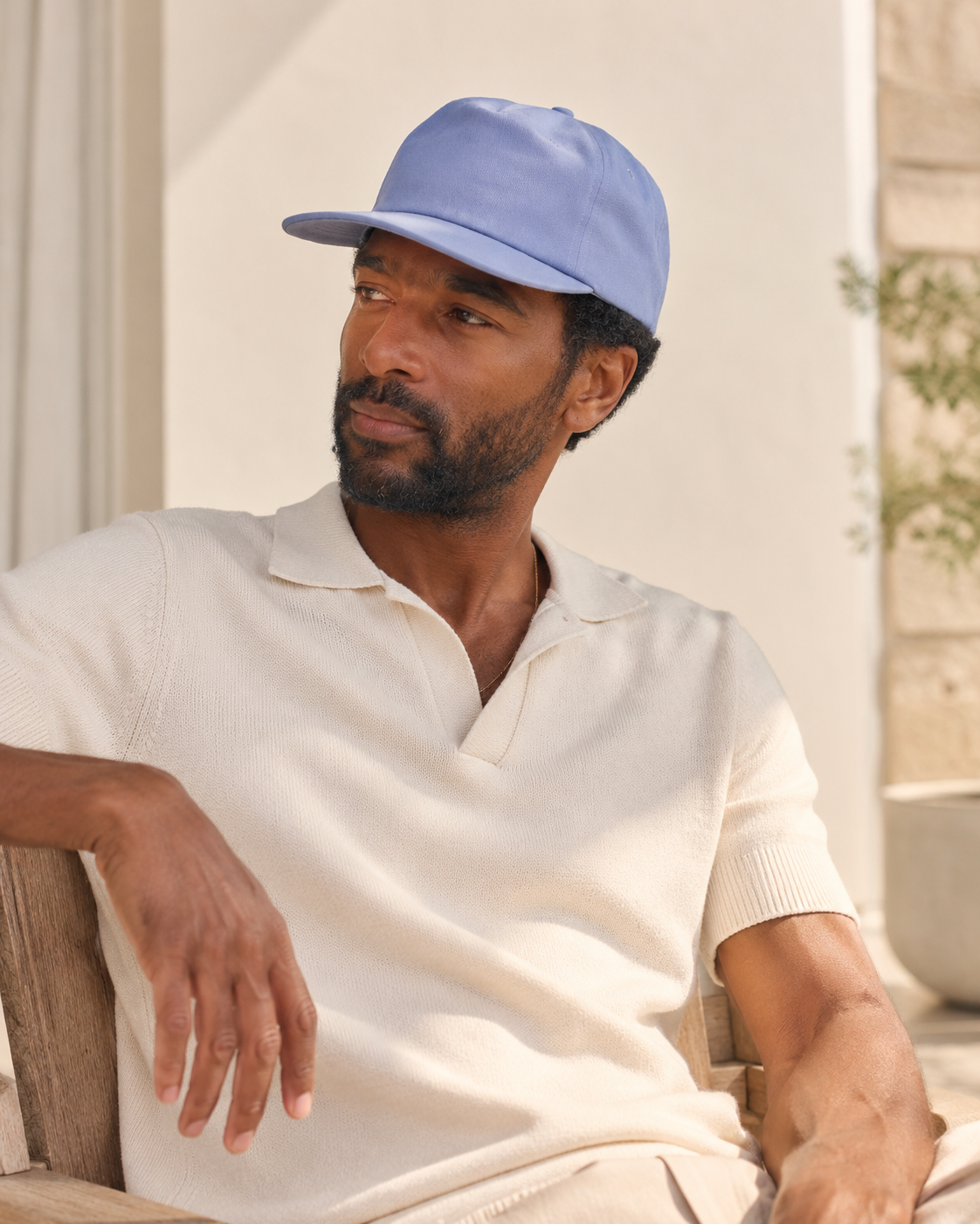 Man wearing a light blue cap and white shirt sitting outdoors.