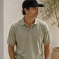 Man wearing a beige polo shirt and black cap standing outdoors with a neutral background