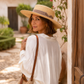 Woman wearing a wide-brimmed hat and white shirt, standing in a sunlit outdoor setting.