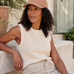 Woman wearing a beige cap and sleeveless top, sitting outdoors.