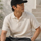Man wearing a black cap and light-colored polo shirt sitting outdoors.