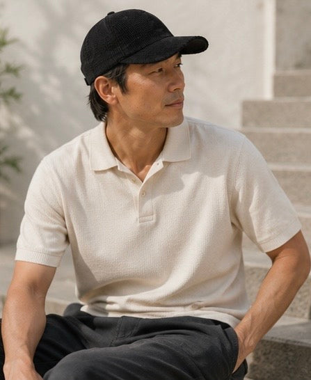 Man wearing a black cap and light-colored polo shirt sitting outdoors.