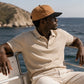 Man wearing a beige cap and shirt on a boat with ocean and mountain background