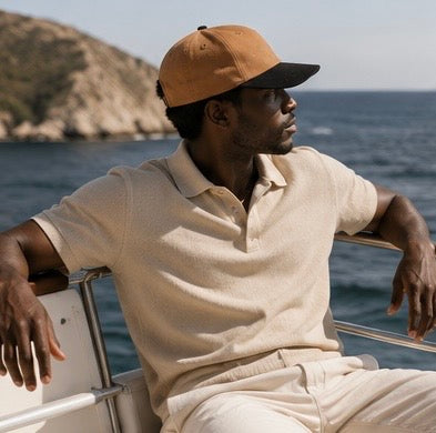 Man wearing a beige cap and shirt on a boat with ocean and mountain background