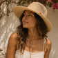 Woman wearing a straw hat and white top outdoors with flowers in the background