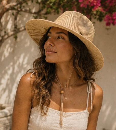 Woman wearing a straw hat and white top outdoors with flowers in the background