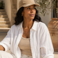 Woman wearing a beige cap and white shirt sitting outdoors.
