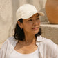 Woman wearing a beige cap and white shirt against a neutral background