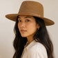 Woman wearing a brown straw hat against a plain background