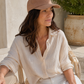 Woman wearing a beige cap and light-colored shirt sitting outdoors.