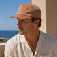 Man wearing a beige cap and light-colored shirt by the ocean