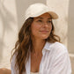 Woman wearing a beige cap and white shirt against a neutral background