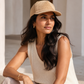 Woman wearing a beige cap and sleeveless top sitting outdoors.