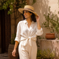 Woman wearing a white shirt and beige pants with a wide-brimmed hat outdoors.