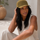 Woman wearing a green cap sitting outdoors with a neutral background
