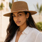 Woman wearing a brown hat and white shirt with a blurred outdoor background