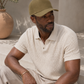 Man wearing an olive green cap and light-colored shirt sitting outdoors.
