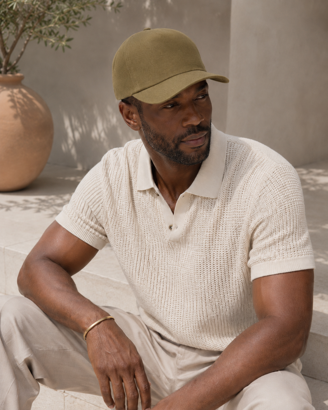 Man wearing an olive green cap and light-colored shirt sitting outdoors.