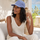 Woman wearing a light blue cap and white outfit sitting outdoors with a scenic background