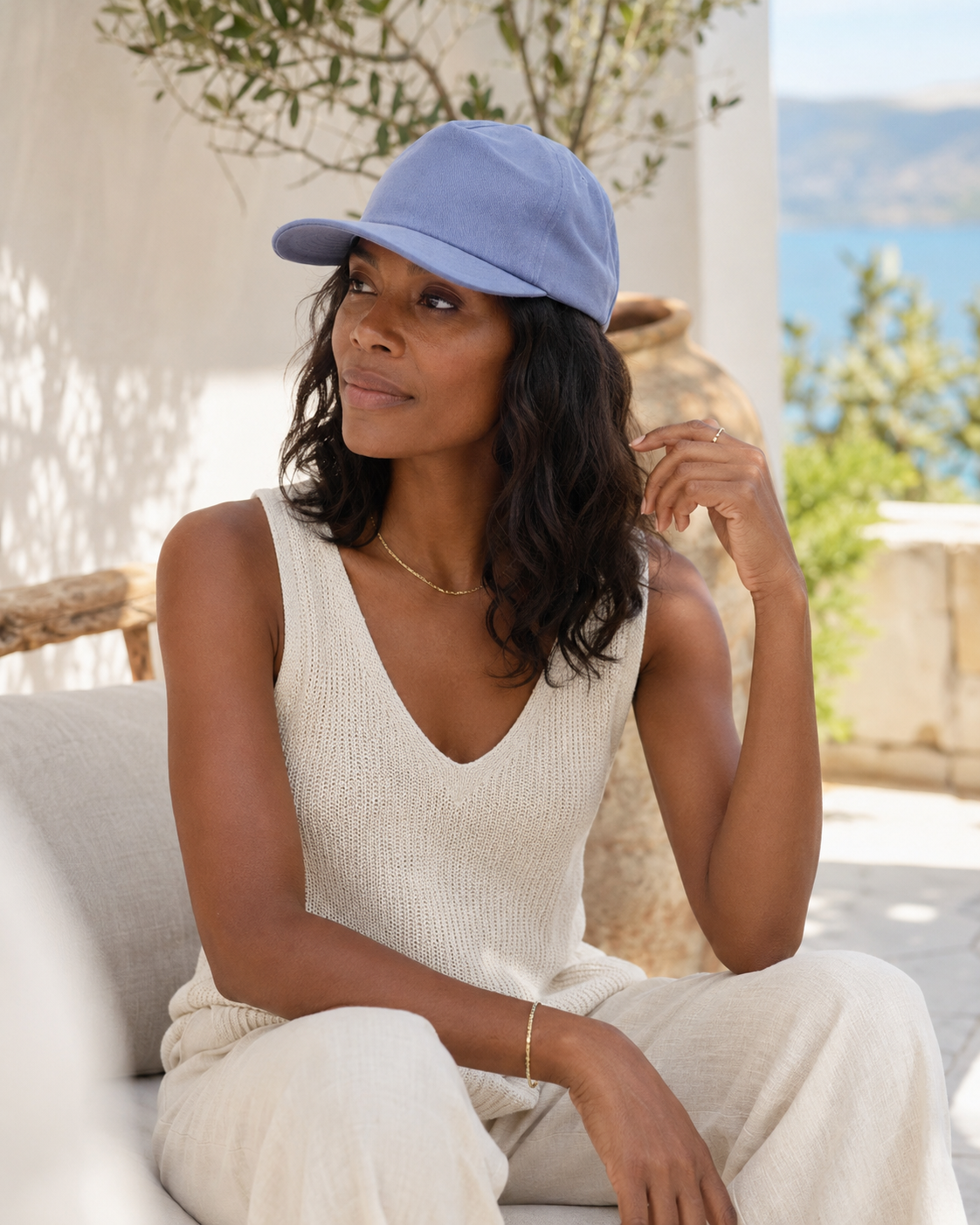 Woman wearing a light blue cap and white outfit sitting outdoors with a scenic background
