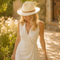 Woman in a white dress and hat standing in a sunlit outdoor setting
