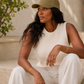 Woman wearing a green cap and white outfit sitting outdoors.