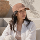 Woman wearing a brown cap sitting outdoors with a neutral background