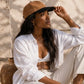 Woman wearing a white shirt and beige pants, sitting outdoors with a brown cap.