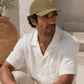 Man wearing an olive green cap and white shirt sitting outdoors.