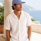 Man wearing a light-colored shirt and blue cap sitting on a ledge with a scenic background.
