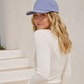 Woman wearing a light blue cap and white outfit against a white wall.