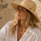 Woman wearing a straw hat and white shirt against a stone wall.